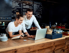 Happy small business owners working with laptop at cafe
